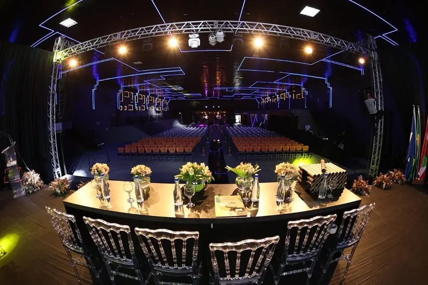 Mesa de honra de formatura no palco da Luna Live, com arranjos de flores e plateia ao fundo